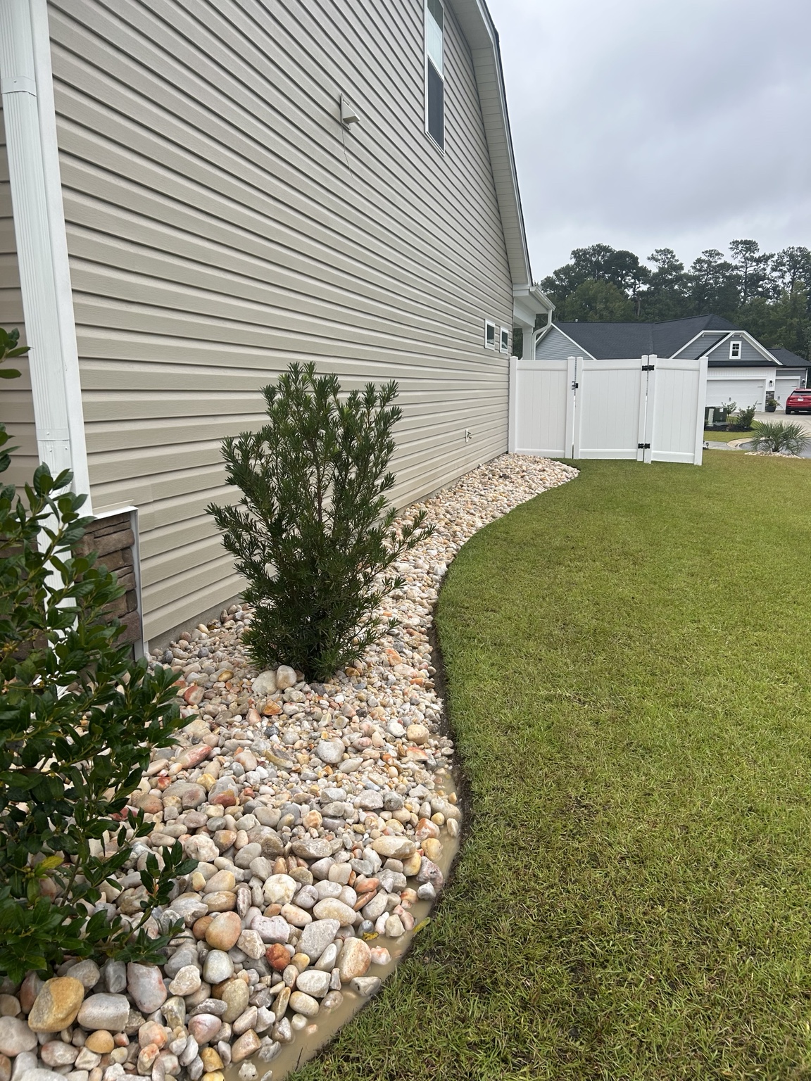 Curved side-yard landscape bed finished with 2 to 5 inch Carolina River Rock